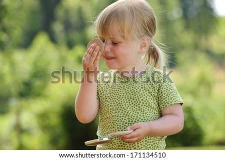 A three year old girl plays with her mother\'s powder compact - she powders her nose