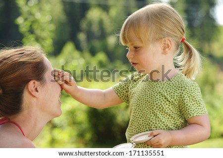 Little girl uses a powder compact to powder her mother\'s face.