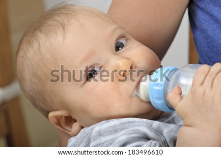 Seven month old baby boy bottle feeding in his mother\'s arms.