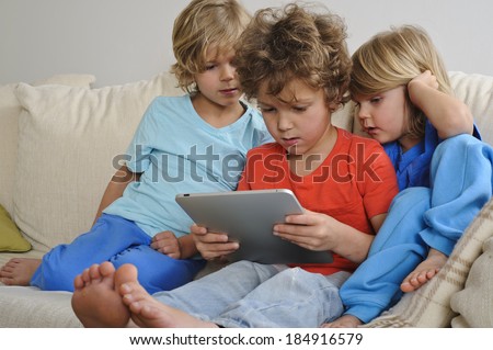 An 8-9 year old is playing a game on a touch screen tablet. His younger brothers are watching every move intently