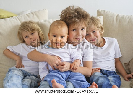 Four brothers, young boys, sitting on a sofa. The eldest is holding a baby in his lap.  They're looking at the camera