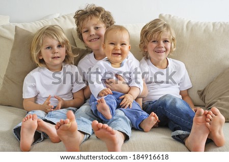Four brothers, young boys, sitting on a sofa. The eldest is holding a baby in his lap.  They\'re looking to the right of camera