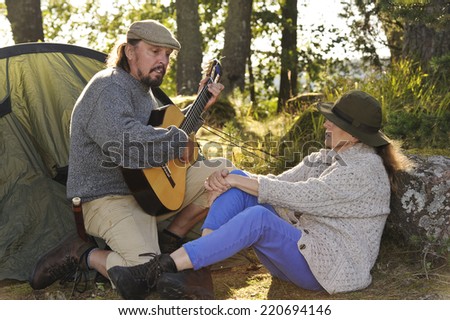 Senior couple enjoying some music outside their tent in evening light. Man plays guitar and sings