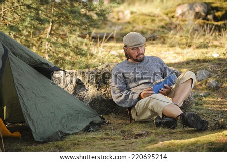 Senior man sits outside a tent and reads a book.