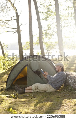 Senior man sits outside a tent and reads a book. There\'s digital filter flare