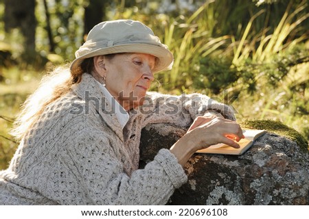 Senior woman sits outside her tent reading a book. There's some digital filter flare