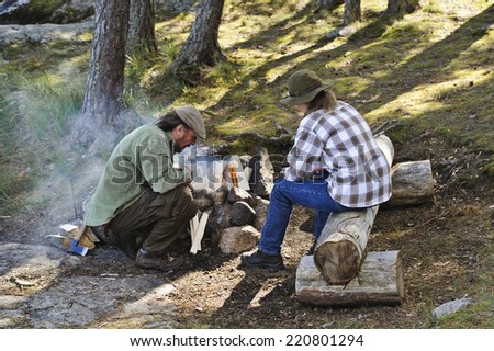 Senior couple light a camp fire. They are in a forest.