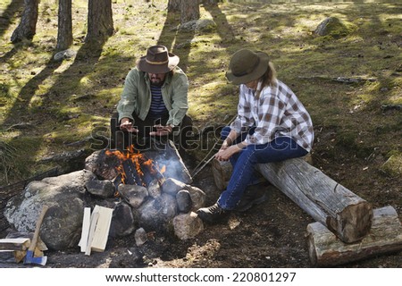 Senior couple sitting by a camp fire. Man warms his hands