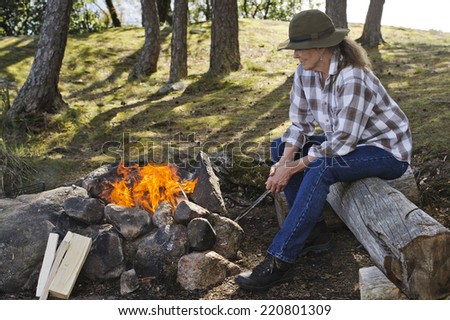 Senior woman sitting by camp fire