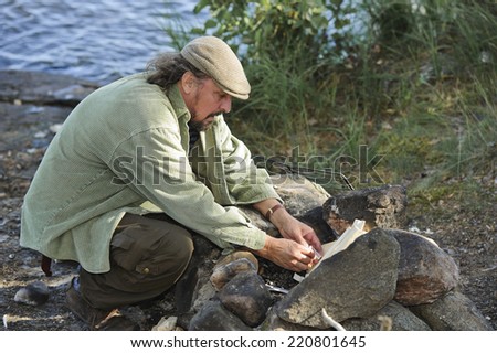 Senior man lights a camp fire with matches.