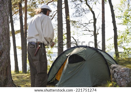 Senior man pitches a tent in forest beside a lake