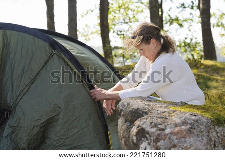 Senior woman pitches a tent in the forest.