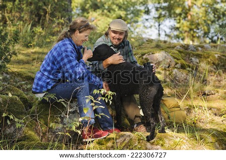 Senior couple playing with their pet dog while out hiking. The dog is a curly haired retriever.Focus is on woman