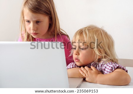 Young boy watches his sister playing a computer game on a laptop. He wishes he could play.