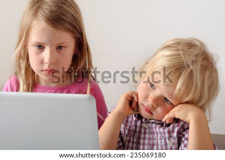 Young boy watches his sister playing a computer game on a laptop. He wishes he could play. Focus on boy. Short depth of field