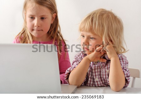 Young boy watches his sister playing a computer game on a laptop. He wishes he could play. Focus on boy. Short depth of field