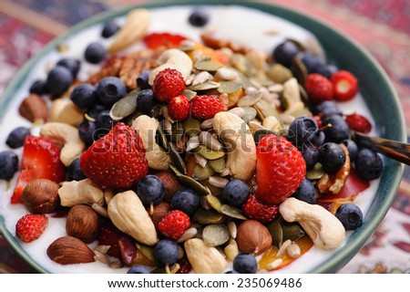 Bowl of yoghurt with strawberries, blueberries, cashew nuts, hazel nuts, pumpkin seeds, and pine nuts. Short depth of field