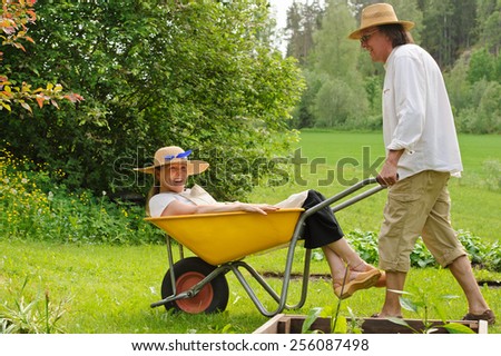 Senior man carries a senior woman in a wheelbarrow . They\'re laughing and having fun.