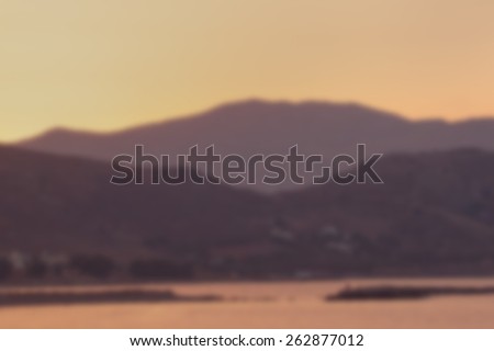 Blurred background of hills and mountains at sunset  with sea in the foreground. Designed to work with text overlays including the text colour white. Artistic intent with filters and desaturation.