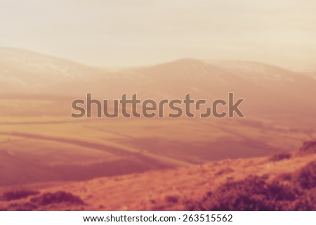 Blurred background, of fields, hills, and mountains. Designed to work with text overlays including the text colour white. Artistic intent with filters and desaturation.