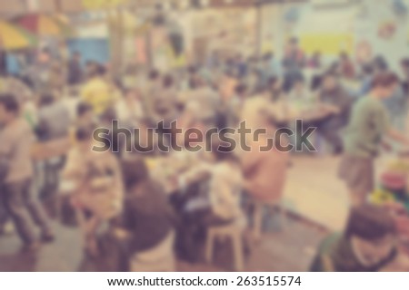Blurred background of many people eating outside in the street. Designed to work with text overlays including the text colour white. Artistic intent with filters and desaturation.