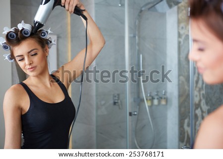 young woman preparing to party having fun, funny girl styling hair with curlers and hairdreyer