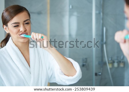 Young pretty woman brushing teeth in front of the mirror