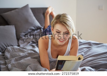 Portrait of a blonde woman reading a book in her bedroom
