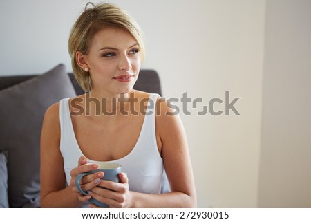 Happy smiling beautiful blond woman awaking with cup of coffee at bedroom