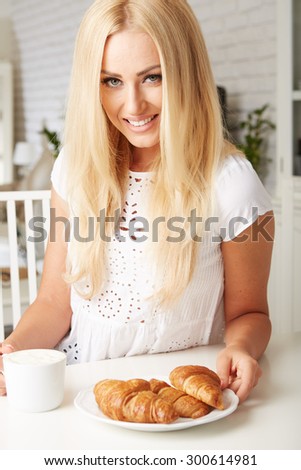 Beautiful young blonde woman enjoying a fresh crispy croissant and a mug of coffee for her breakfast