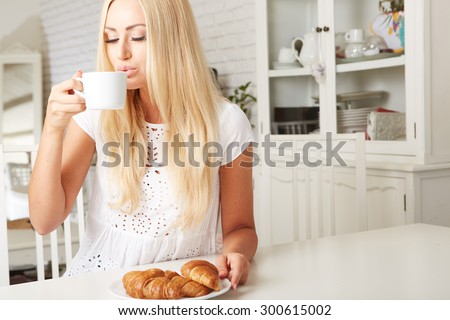Beautiful young blonde woman enjoying a fresh crispy croissant and a mug of coffee for her breakfast