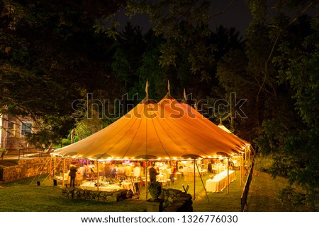 a wedding tent at night surrounded by trees with an orange glow from the lights, long exposure - wedding tent series