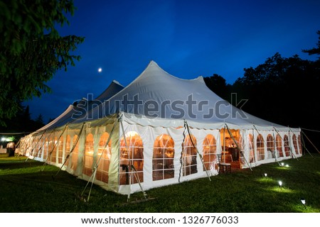 A wedding tent at night with blue sky and the moon. The walls are down and the tent is set up on a lawn - wedding tent series