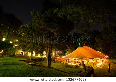 a wedding tent at night surrounded by trees with an orange glow from the lights. - wedding tent series