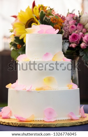 White wedding cake with yellow and pink rose petals and flowers in the background - wedding cake series