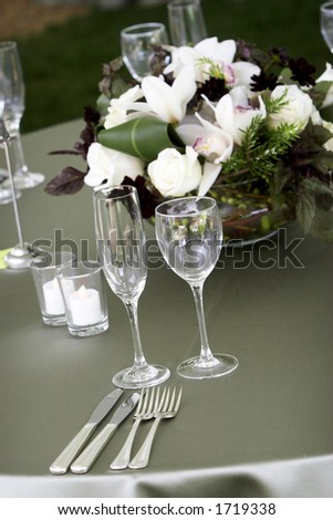 a typical dinner table setting, with a shallow depth of field with the focus on the glasses and silverware, flowers out of focus