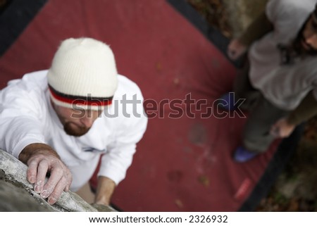 A rock climber reaches for a hand hold while his friend looks on. There is lots of room for text in this image, as the focus is on the hand in the lower left corner of the frame.
