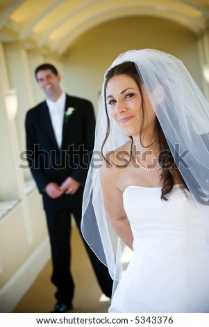 Bride and groom with the man standing in the background. Shallow depth of field, dark haired woman with a smile.