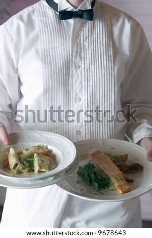 A waiter holds two plates of tasty food.