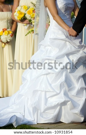 brides dress during the wedding ceremony in white with yellow bridesmaids in the background