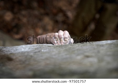 A climber makes his way to the top. His hand is covered in chalk, and there is a very shallow depth of field. The white specks are small pieces of chalk dust flying through the air.