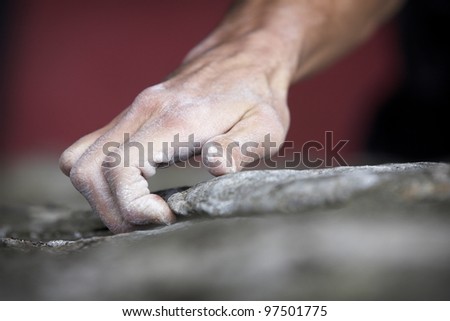 Grabbing onto a small handhold, a climber makes his way to the top. His hand is covered in chalk, and there is a very shallow depth of field.