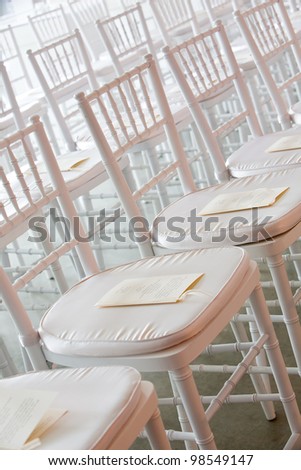 Fancy white chairs set up during a wedding ceremony. There is paper with the schedule on it. You cannot read the words.