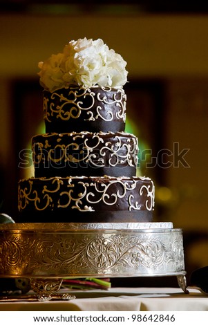 A chocolate wedding cake with white frosting details and flowers on top