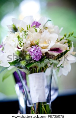 A brides wedding bouquet of flowers sitting in a vase full of water. Very shallow depth of field, focus on the purple flowers