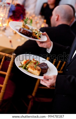 a waiter serving plates of food at a catered wedding