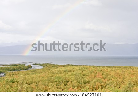 Rainbow over a mountain lake. Autumn, fall colors in the forest. Mountains in the background.