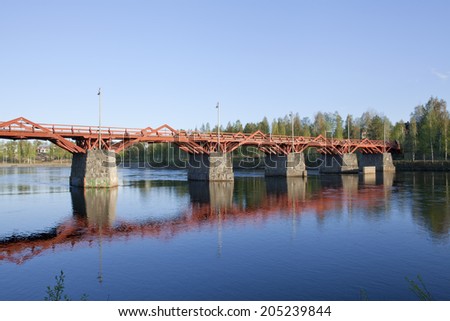 Red wooden, glued laminated timber bridge crosses a river in evening lit. Lejonstromsbron in Skelleftea.