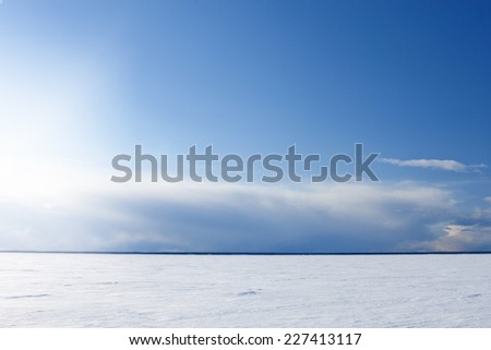 Ice and snow on a bright sunny sea, ocean. Shoreline far away in the white winter distance. Clouds, shower in the background of a blue sky.