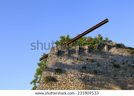 Rusty metallic iron beam, which is situated on a rusty metal ball, high above you, on a stone wall!